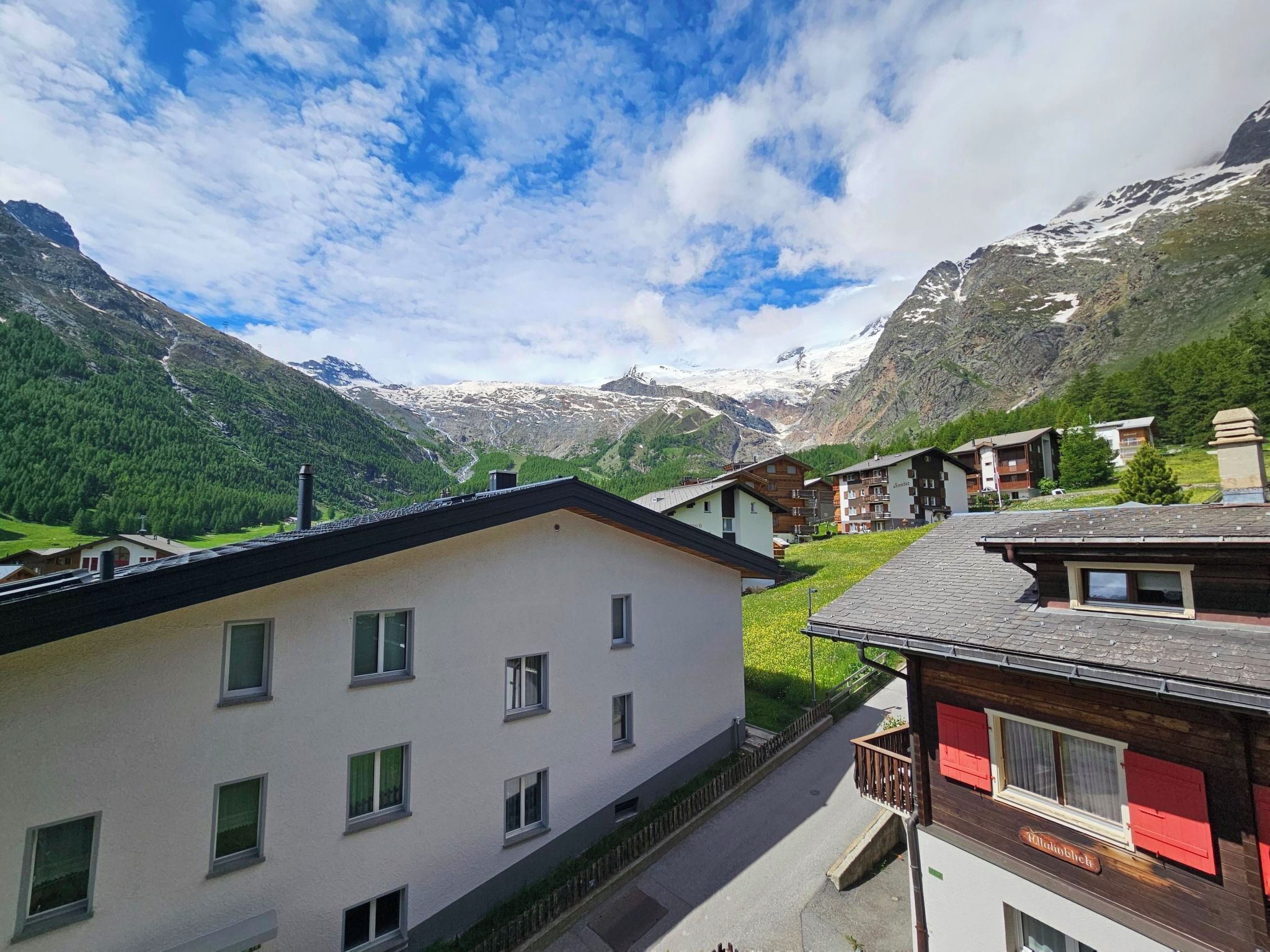 Un village de montagne avec des bâtiments, un ciel dégagé et des sommets enneigés en arrière-plan.