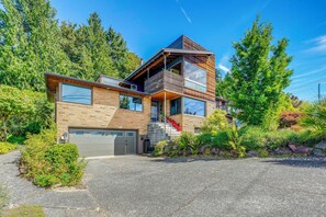A modern two-story house with a garage, surrounded by lush greenery and trees. - 1/2 Mi to Alki Beach + Puget Sound Views! (Seattle)
