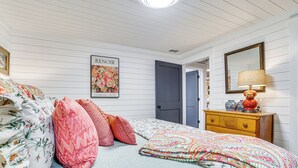 Een slaapkamer met een bed, kussens, een dressoir, een lamp, een spiegel en een poster aan de muur.