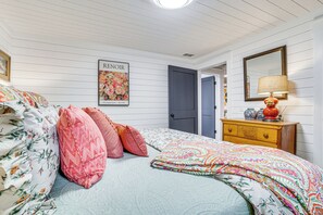 Ein Schlafzimmer mit Bett, Kissen, Kommode, Lampe, Spiegel und einem Poster an der Wand.