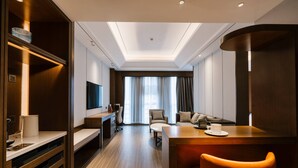 Ein modernes Hotelzimmer mit einem Holztisch, einer Couch, einem Fernseher und einem großen Fenster mit Vorhängen.