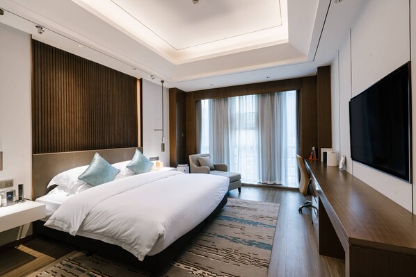 A modern hotel room with a large bed, a desk, a television, and a large window with curtains.