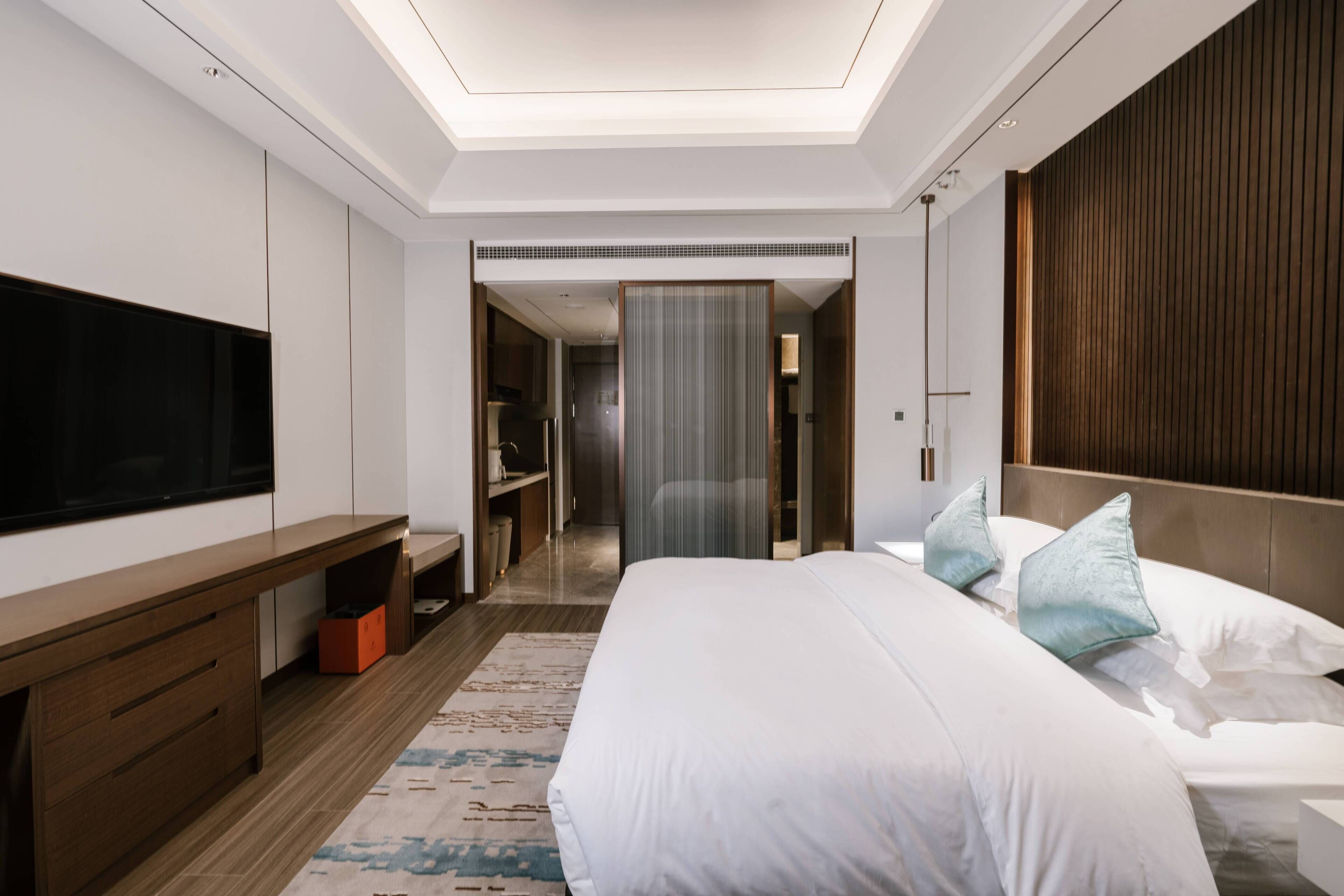 Una habitación de hotel moderna con una cama grande, un televisor de pantalla plana, un aparador de madera y un vestidor.