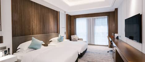 A hotel room with two beds, a desk, a chair, a television, and a large window.