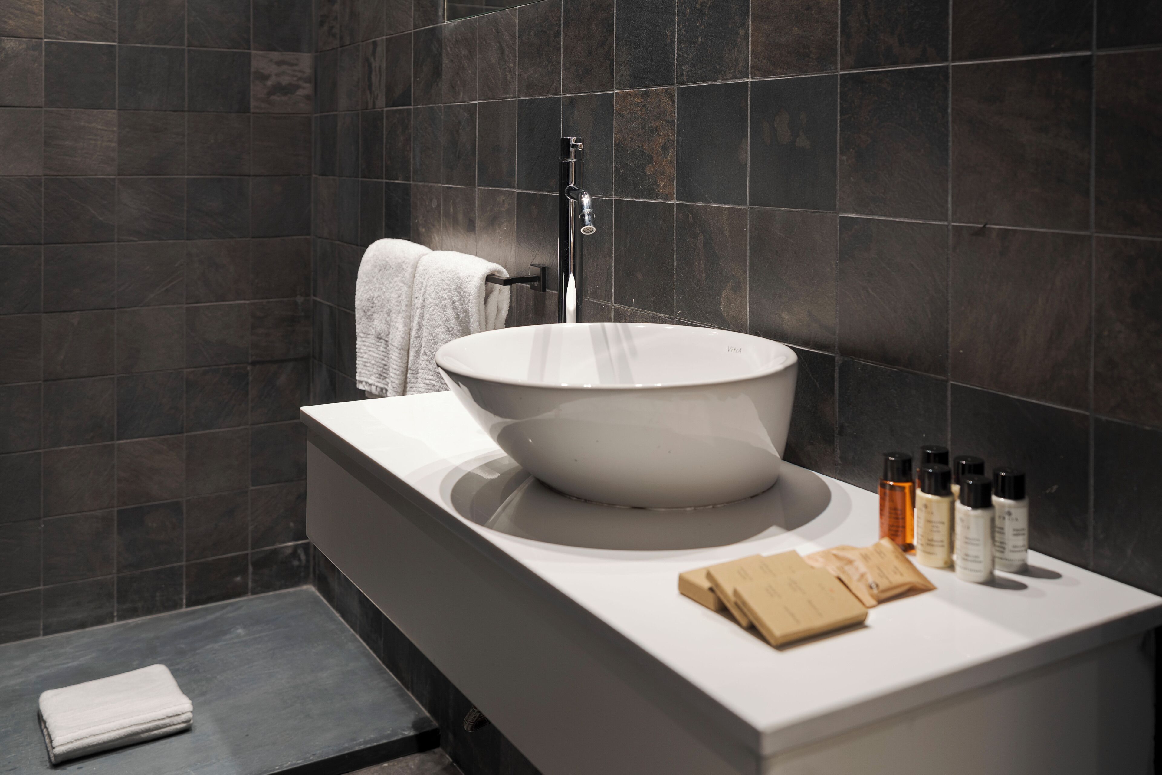 A modern bathroom with a large vessel sink, a towel rack, and toiletries on the countertop.