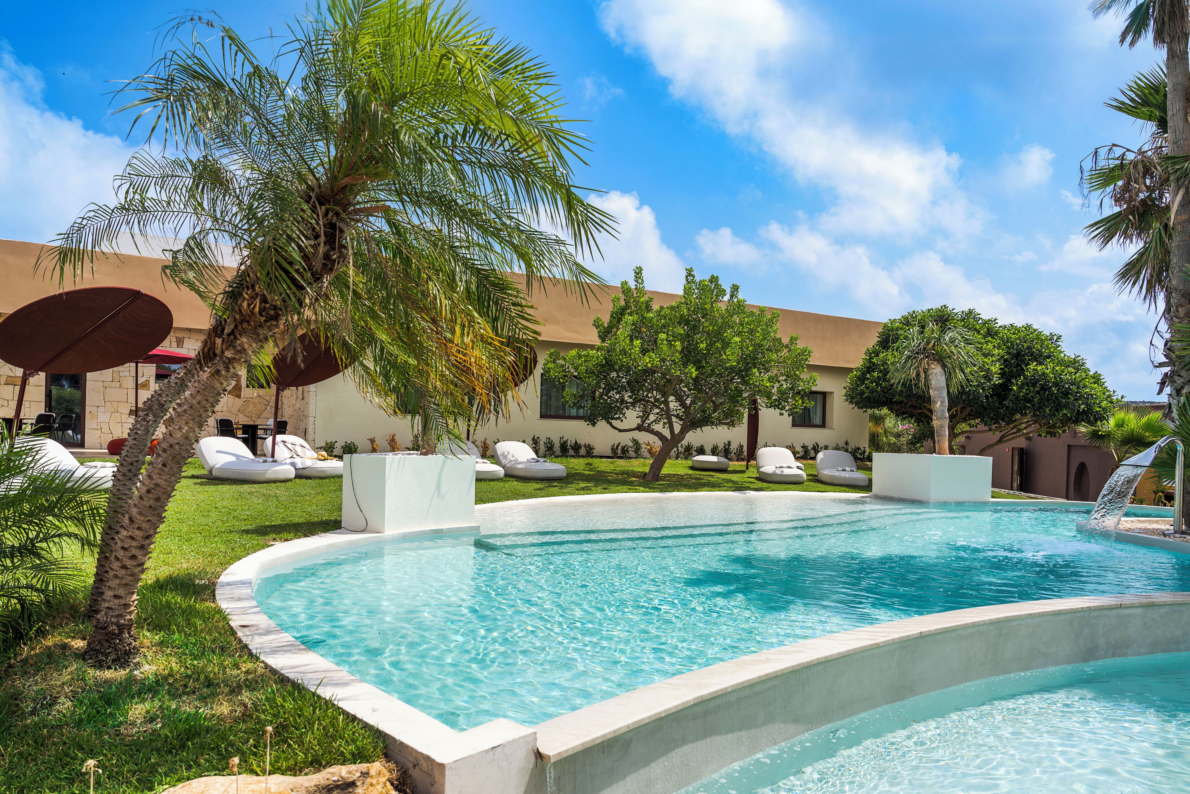 A swimming pool with lounge chairs and palm trees.