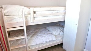 Uma cama box com escada, beliche inferior com colchão e almofadas, e um guarda-roupa branco.