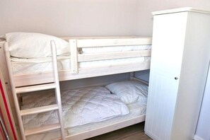Ein Stockbett mit einer Leiter, eine untere Schlafstelle mit einer Matratze und Kissen sowie ein weißer Kleiderschrank.