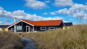 En bygning ved kysten med rødt tag, store vinduer og en sti, der fører hen til den.