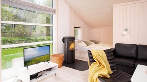 Et hyggeligt værelse med seng, fjernsyn, pejs og et vindue med udsigt over grøn vegetation.