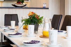 Ein Frühstückstisch mit einer langen Tafel, weißen Tellern, Tassen und einem Orangensaftkrug.