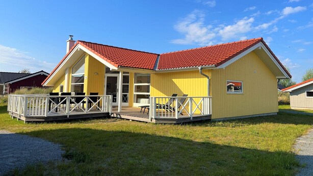 En gul bygning med rødt tag, en overdækket terrasse og et lille vindue.