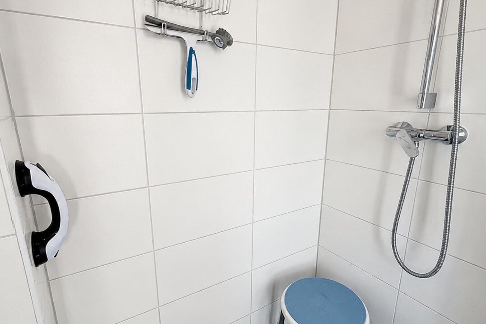 Ein Badezimmer mit weißen Fliesen, einer Dusche, einer Toilette und einem Handtuchhalter.