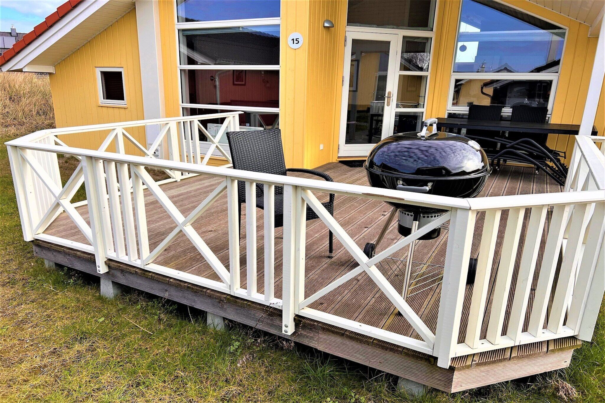 Une terrasse avec une rambarde blanche, un barbecue et du mobilier d’extérieur.