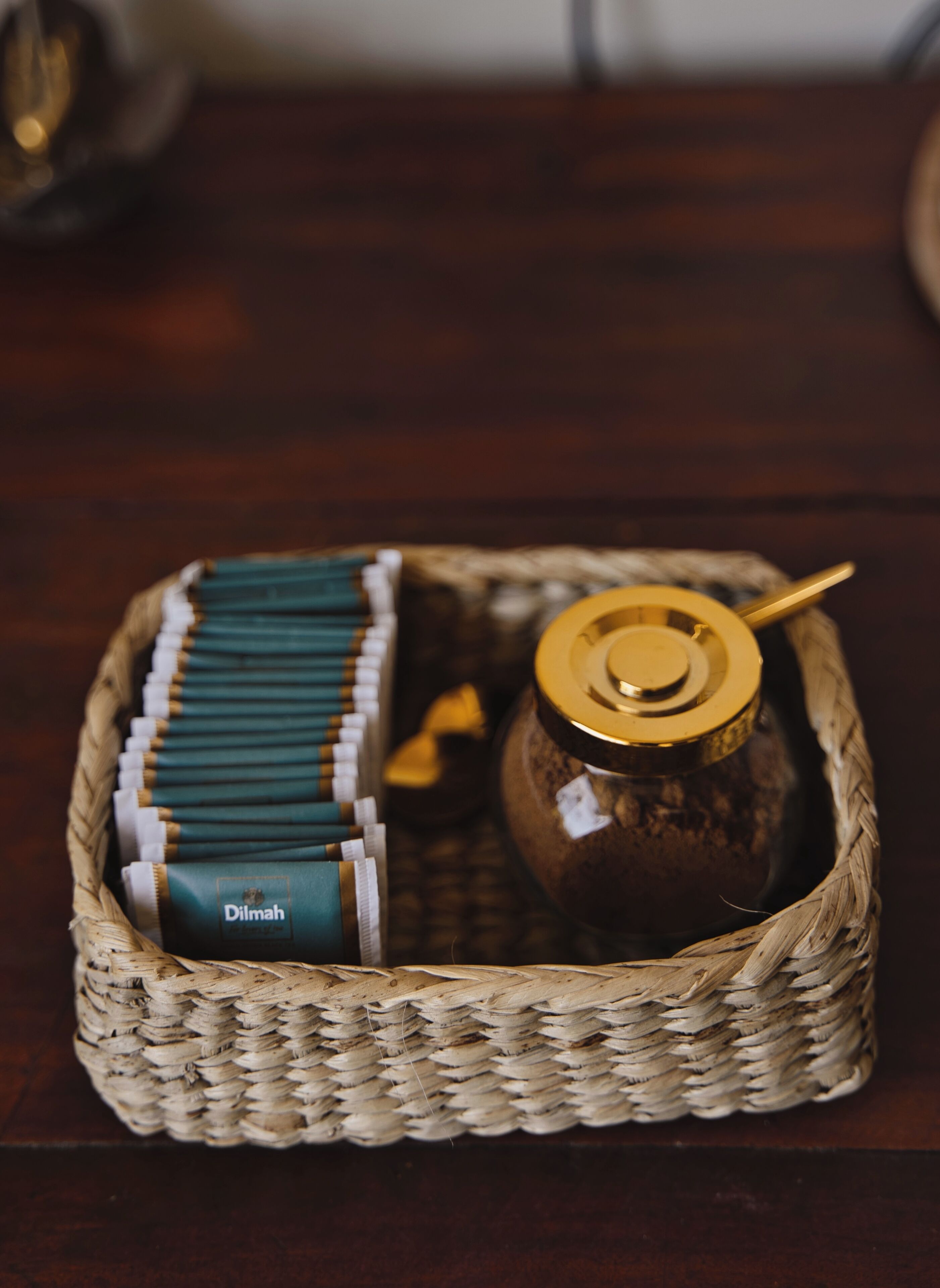 Een gevlochten mand met een pot met gouden deksel en een stapel verpakte groene en witte producten.