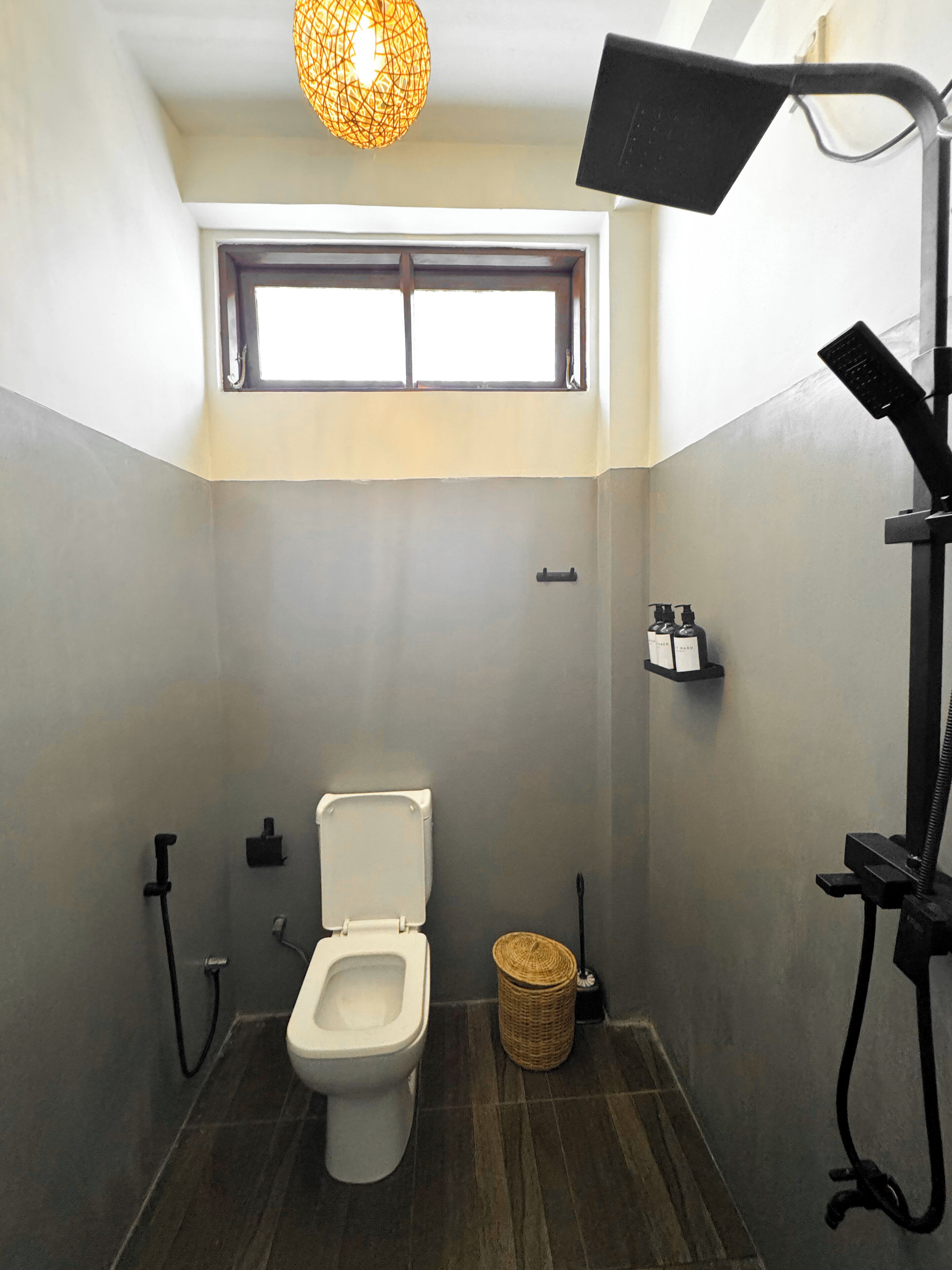 Un baño con inodoro, ventana, repisas con artículos de aseo y zona de ducha.