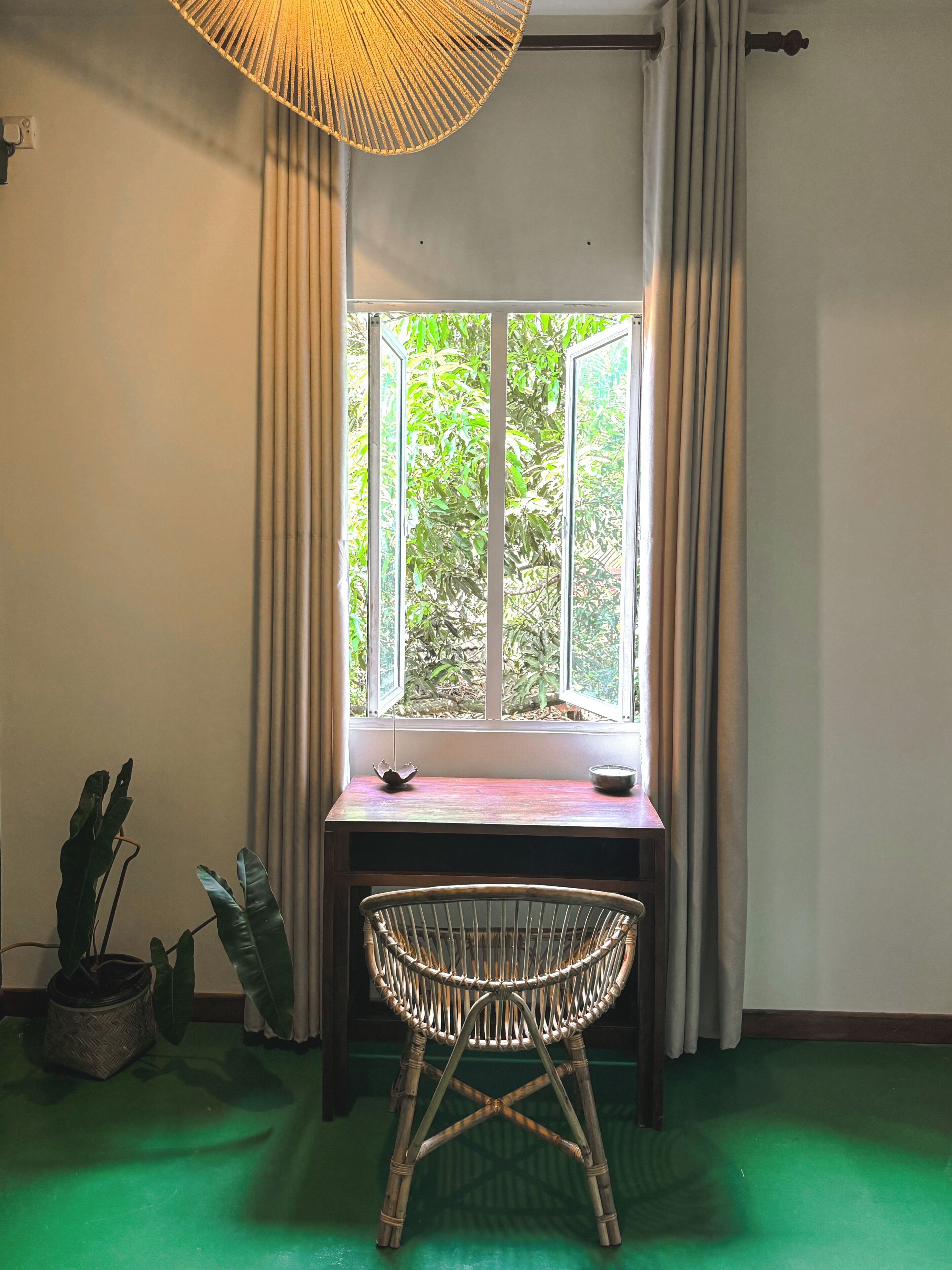A room with a window, a table, a chair, and a hanging light fixture.