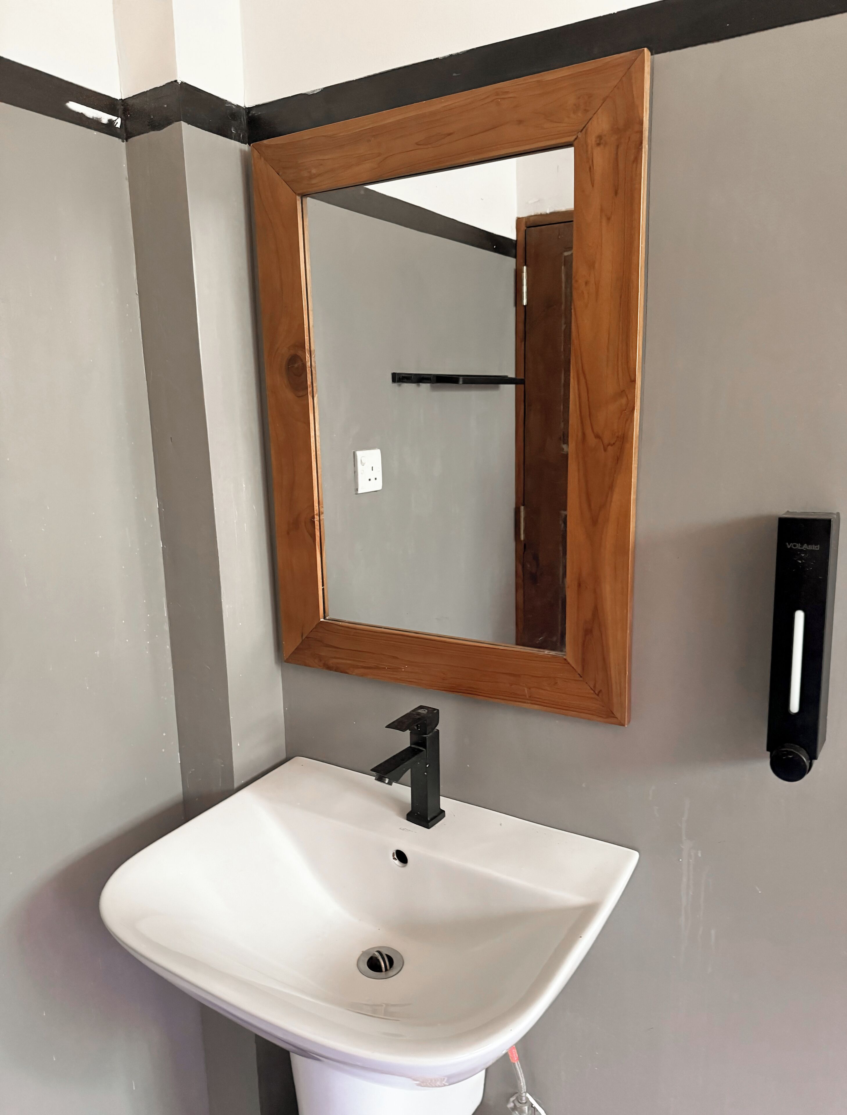 A bathroom with a white sink, a wooden-framed mirror, and a black wall-mounted faucet.