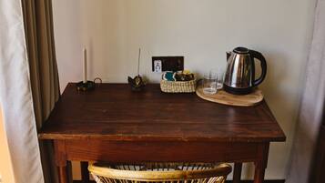 A wooden table with a wicker chair in front, a candle, a kettle, and a basket on the table.