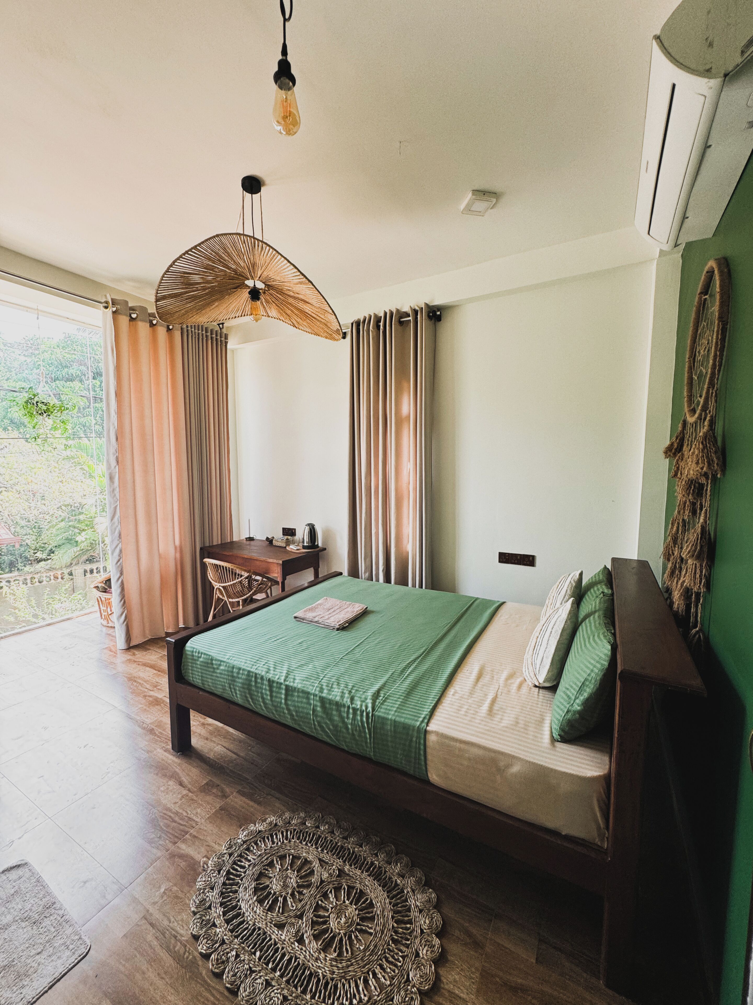 A bedroom with a bed, a desk, a chair, and a view of greenery outside.