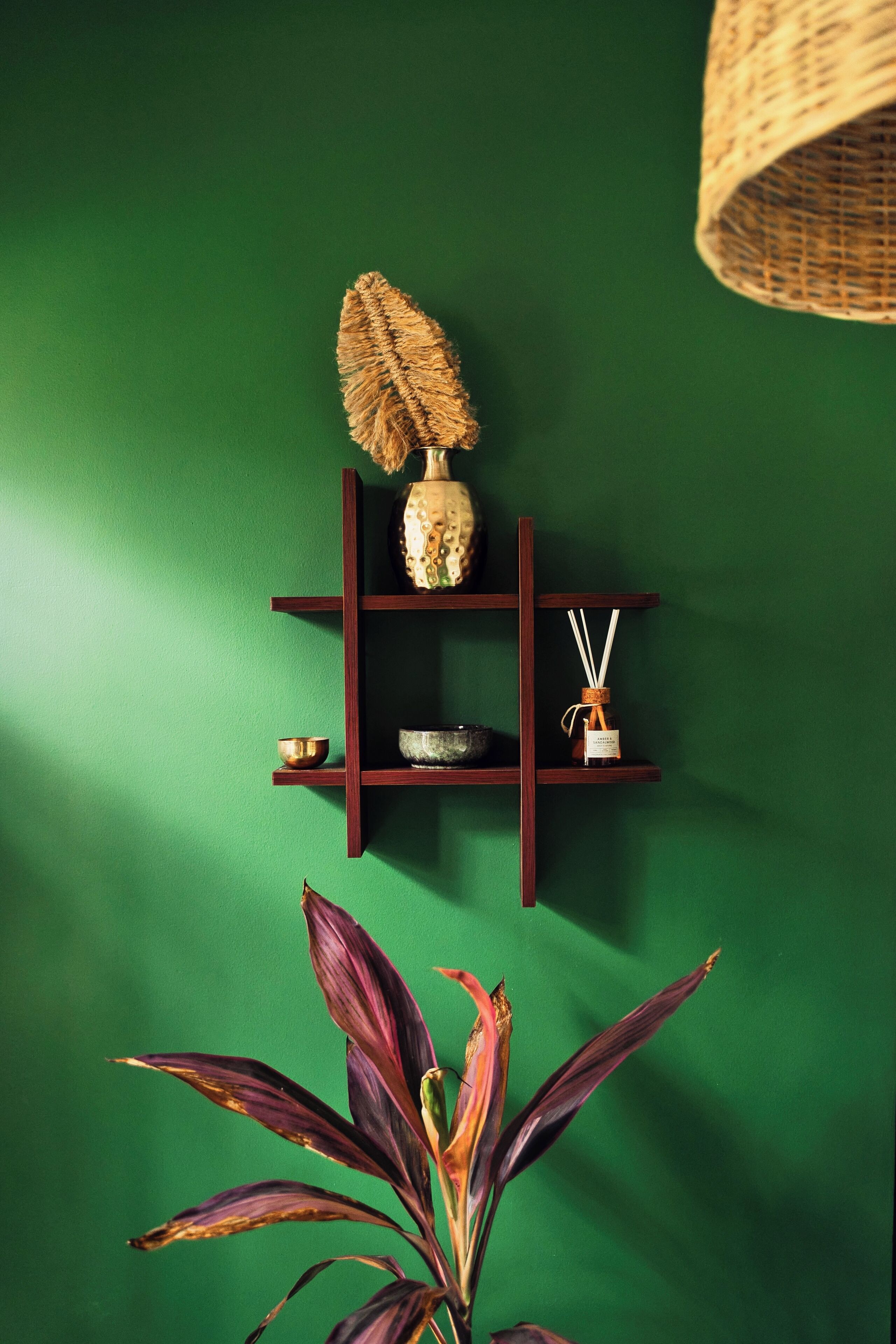Een groene muur met een houten plank waarop een vaas, een schaal en een fles staan.