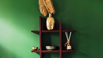 Een groene muur met een houten plank waarop een vaas, een schaal en een fles staan.