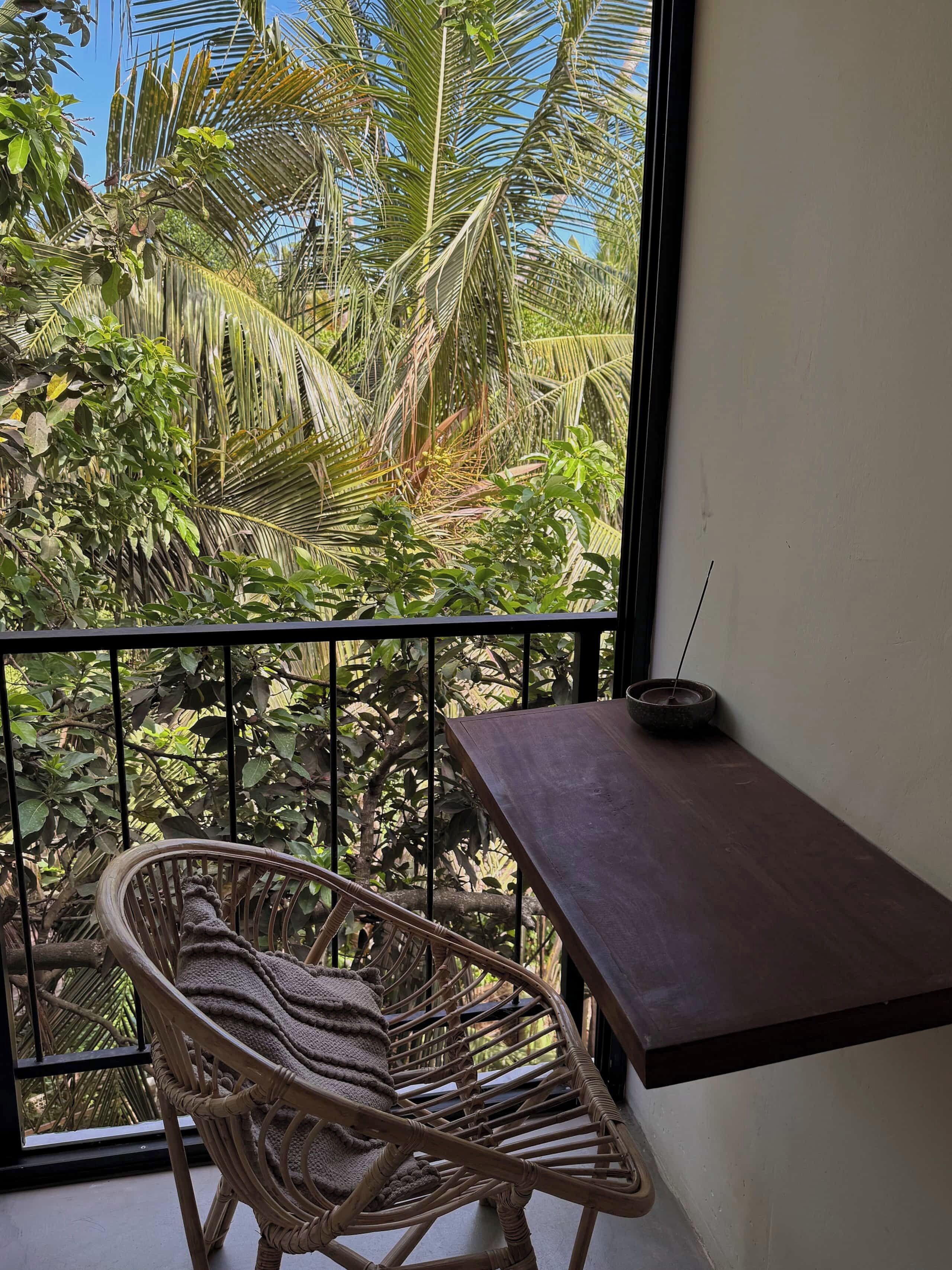 A wicker chair with a cushion on a balcony with a view of tropical foliage.