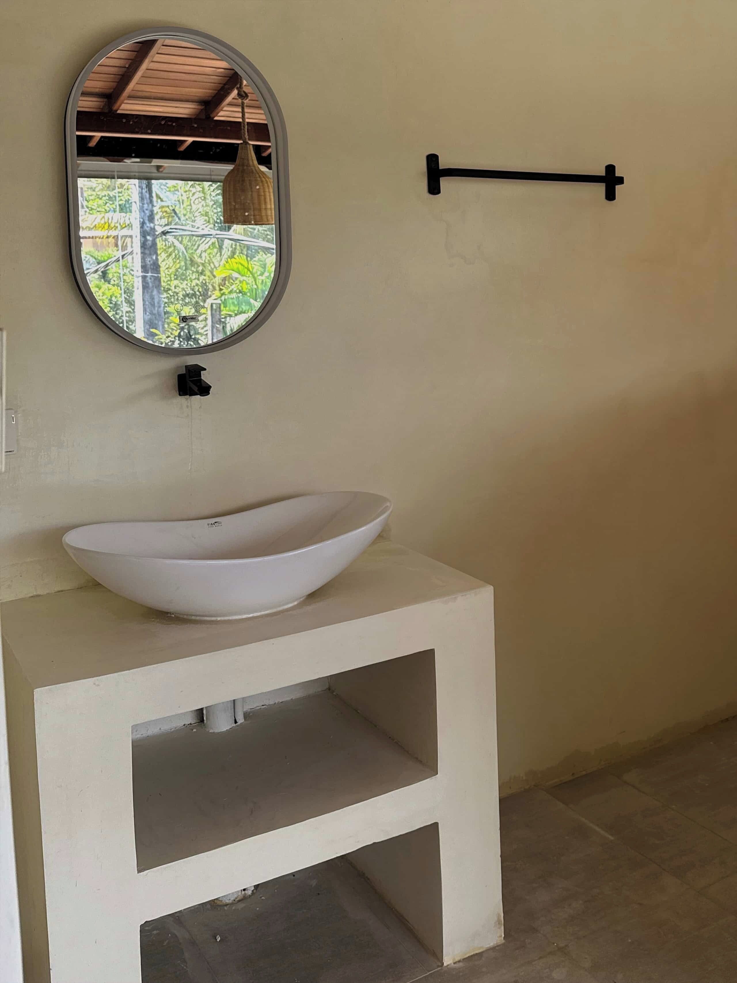Un baño con un lavamanos blanco, un espejo y un perchero para toallas.