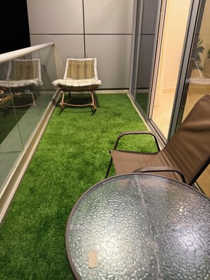 Ein Balkon mit künstlichem Rasen, einem Glastisch und zwei Korbstühlen.