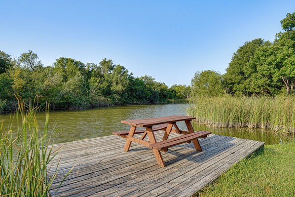 A wooden picnic table on a dock by a river with trees in the background. - Boat Dock & Ramp! Brazos River Couple’s Retreat (Granbury)