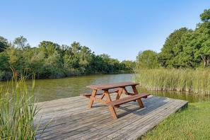 A wooden picnic table on a dock by a river with trees in the background. - Boat Dock & Ramp! Brazos River Couple’s Retreat (Granbury)