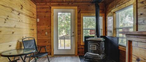A wooden cabin interior with a door, a table with chairs, and a wood-burning stove.