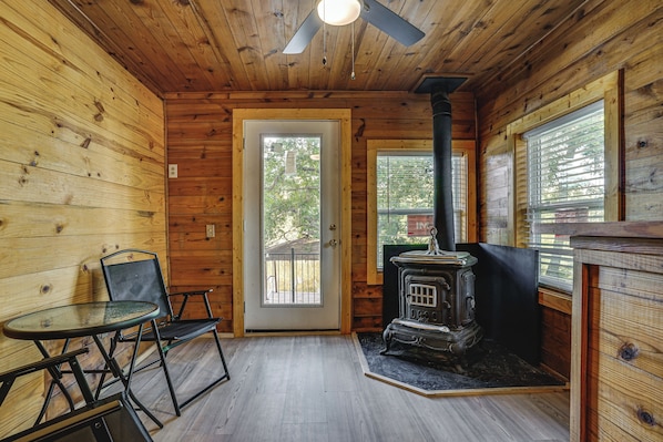 Interior de uma cabana de madeira com porta, uma mesa com cadeiras e um fogão a lenha.
