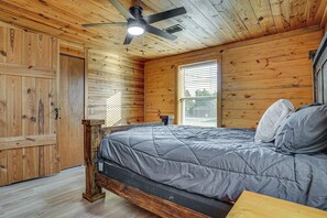 A wooden-paneled bedroom with a bed, a ceiling fan, and a window. - Boat Dock & Ramp! Brazos River Couple’s Retreat (Granbury)