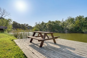 A wooden picnic table on a dock with a body of water and trees in the background. - Boat Dock & Ramp! Brazos River Couple’s Retreat (Granbury)