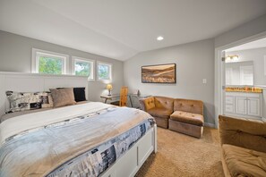 Ein Schlafzimmer mit einem großen Bett, einem Schreibtisch, einem Sessel und einer Couch. Es gibt ein Fenster und ein Bild an der Wand.