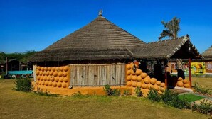 Una cabaña tradicional con techo de paja y puerta de madera, rodeada por un muro bajo y un pequeño jardín.