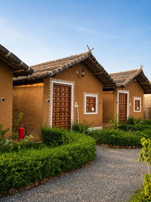 A traditional building with a thatched roof, a red barrel, and a gravel path.