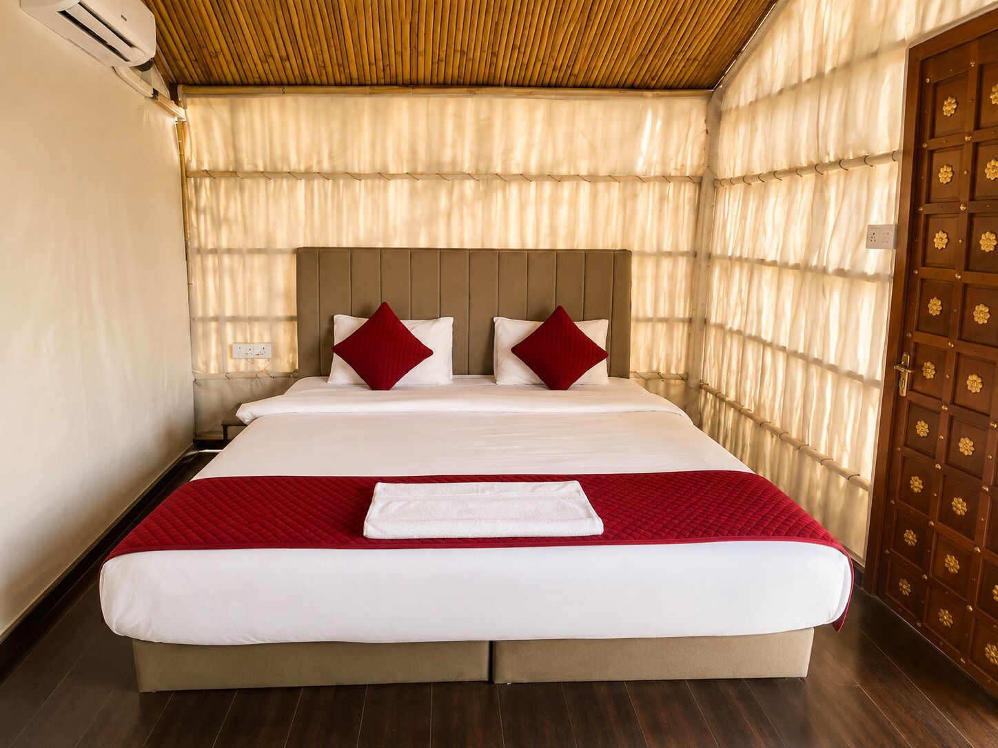 Una habitación de hotel con una cama grande, un cabecero de madera y una puerta de madera con motivos florales.