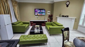 A living room with green sofas, a coffee table, a TV, and a fireplace.