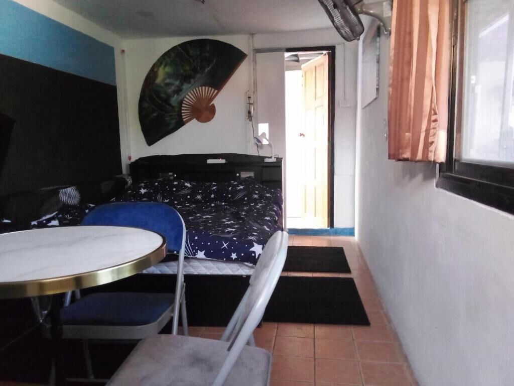 Ein gemütlicher Raum mit Bett, kleinem Tisch, Stuhl und Wandventilator.