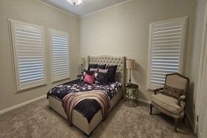 A bedroom with a bed, a chair, and two windows with blinds.