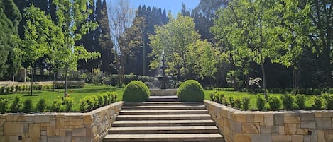 A stone staircase leading to a fountain in a well-maintained garden with trimmed hedges and trees.