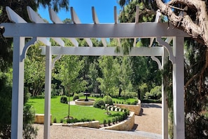 A garden with a white pergola structure, well-maintained grass, and various shrubs.