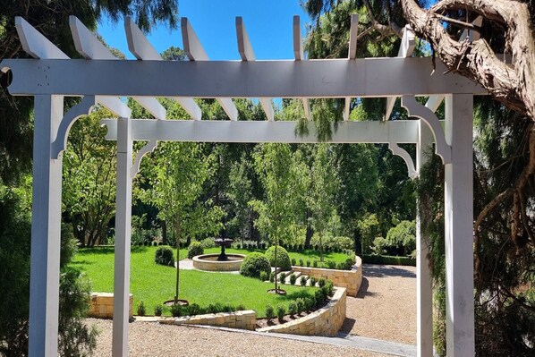 A garden with a white pergola structure, well-maintained grass, and various shrubs.