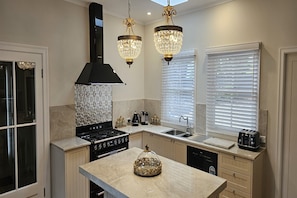 A modern kitchen with a central island, a black range hood, and two crystal chandeliers.