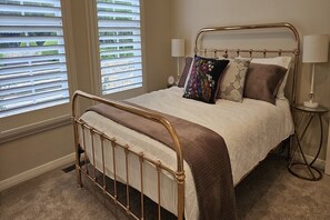 A bed with a metal frame, a bedside lamp, and a window with blinds.