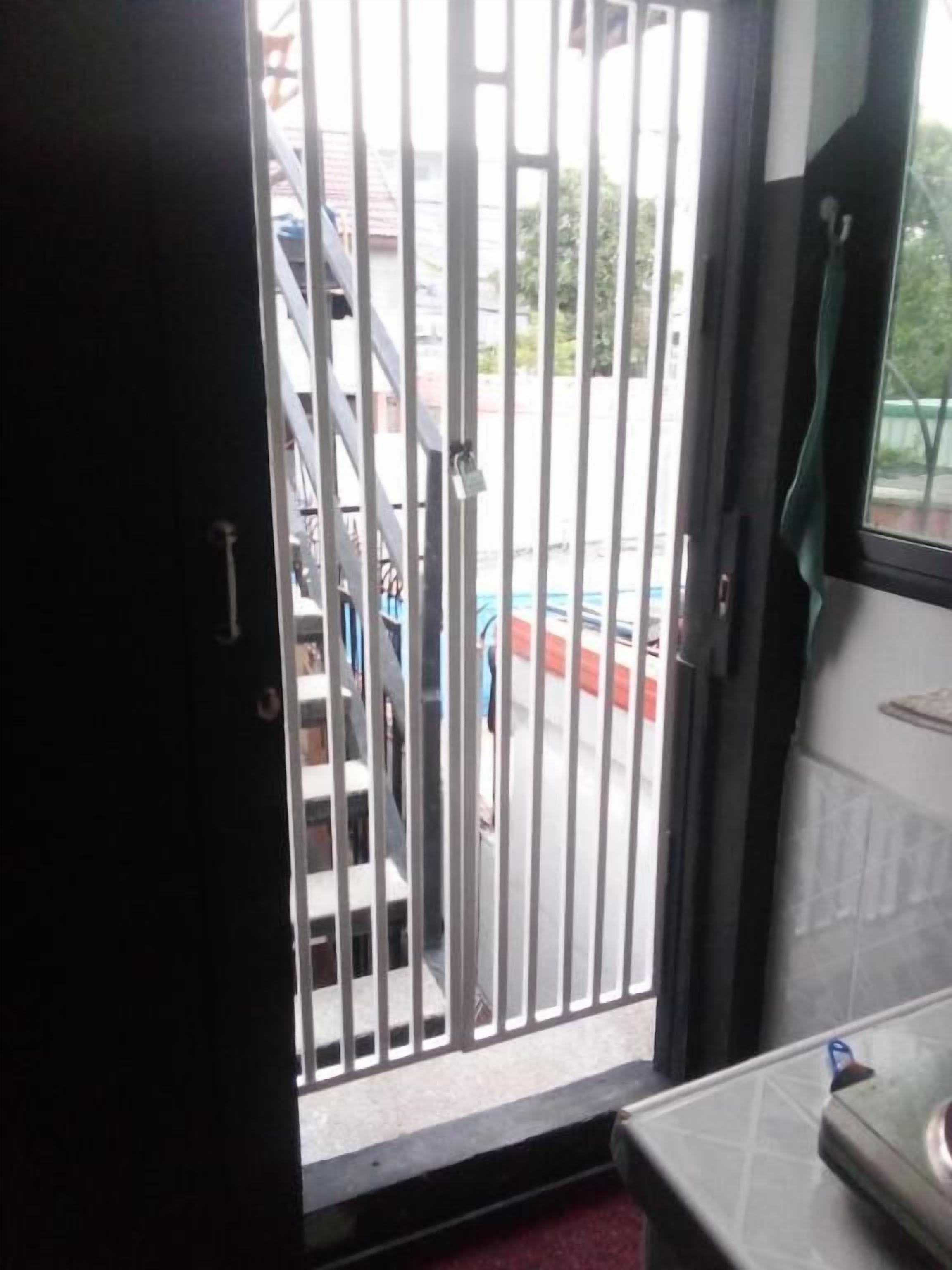 Vista a través de una reja metálica hacia un estacionamiento, con un edificio al fondo.