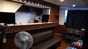 Quarto com sofá, ventoinha, cozinha equipada com micro-ondas e janela com cortinas.