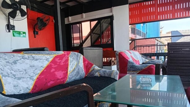 Un coin salon avec une table en verre, des fauteuils confortables aux tissus colorés et un ventilateur fixé au mur.